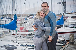 Guy cuddles with a blonde girl among yachts on a gray wooden pier