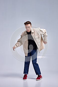 Guy dancing contemporary dance in studio, grey background. Acrobatic male dancer