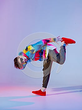 Guy dancing contemporary dance in studio. Neon light grey background. Acrobatic bboy dancer. Break dance lessons.