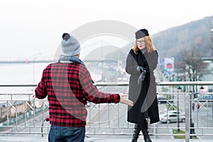 Guy delayed to date. Woman shows to watches on arm. Man spread his arms. Delayed dated on bridge.