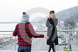 Guy delayed to date. Woman shows to watches on arm. Man spread his arms. Delayed dated on bridge. photo