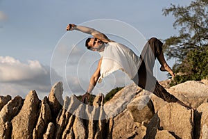 Guy doing yoga poses on sharp rocks near the beach in thailand