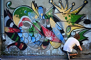 The guy draws on the graffiti wall a drawing with aerosol paints of various colors