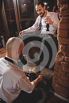 Guy drinking beverage and looking on shoeshiner