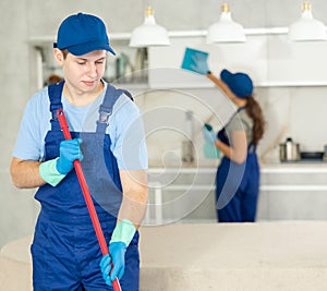 Guy employee of cleaning company in blue jumpsuit cleans and washes floor in kitchen