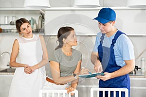 Guy employee of repair team in blue overalls submits to female client document on payment