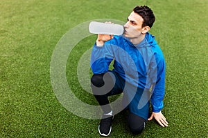 Guy after exercise, drinking water on the football field. Portrait of beautiful Guy in sportswear.