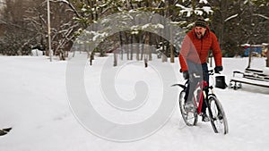 A guy falls off his bike in a winter park