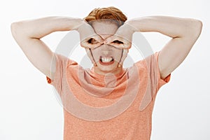 Guy feeling like superhero. Portrait of funny joyful and childish pretty boy with freckles and red hair, making mask