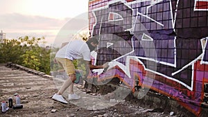 Guy finishing painting graffiti on wall with an aerosol, side view. Talented young graffiti artists painting. Male