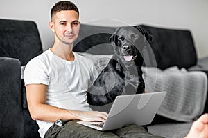 Guy freelancer with his dog labrador playing at home