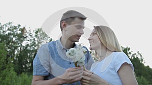 The guy and the girl blow on dandelions