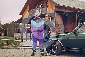 Guy and girl in clothes of the nineties, next to the old car