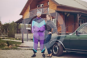 Guy and girl in clothes of the nineties, next to the old car