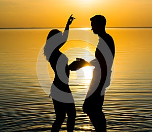 The guy and the girl are dancing at sunset background, silhouettes