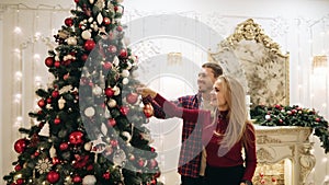 The guy and the girl decorate the Christmas tree and dropped the ball