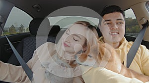 A guy and a girl are driving in a car with a cat and a dog. The girl shows the guy something funny on the phone. People