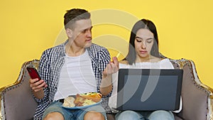 The guy and the girl are eating fast food, the girl is sitting at a laptop, and the guy is looking at the phone, on a