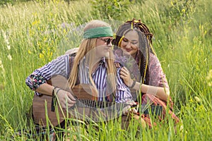 Guy and a girl in hippie style with a guitar are sitting in the grass on a forest glade