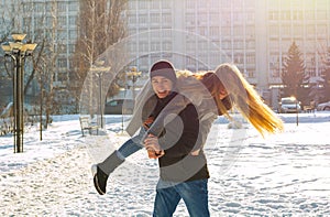 The guy and the girl indulge in the winter, he holds her on his shoulders and turns. A loving couple is playing outside