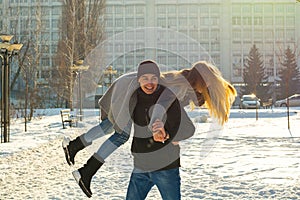 The guy and the girl indulge in the winter, he holds her on his shoulders and turns. A loving couple is playing outside
