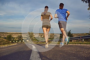 A guy and a girl jog along the road in nature.