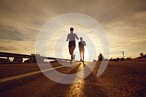 A guy and a girl jog along the road at sunset in nature.