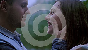 A guy and a girl look into each other`s eyes. the guy is holding the girl`s hands behind his face. Close up