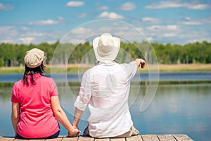 Guy and girl look at the lake sitting on the pier, view from the