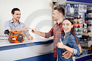 The guy and the girl pay for the purchase of a chainsaw.