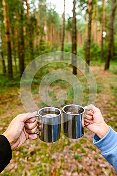 A guy and a girl on a picnic in the forest are holding mugs of tea.