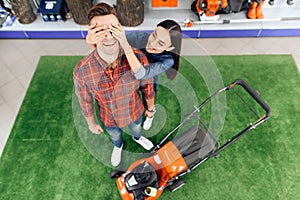 A guy and a girl are posing on the camera with a lawn mower.