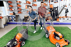 A guy and a girl are posing on the camera with a lawn mower.