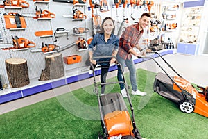 A guy and a girl are posing on the camera with a lawn mower.