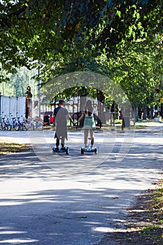 A guy and a girl ride a hoverboard with their backs in the park and hold hands