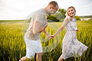 The guy and the girl are running on the green grass and smiling.