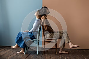 Guy and girl sit back to back on a chair. Background is divided into two halves.