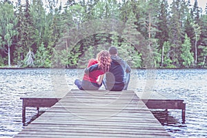 Guy and a girl sit hugging on the pier of a beautiful lake. The concept of love, the summer mood