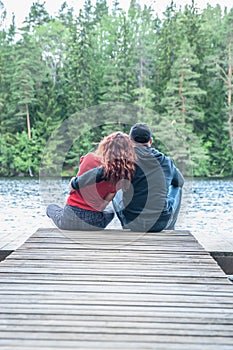 Guy and a girl sit hugging on the pier of a beautiful lake. The concept of love, the summer mood