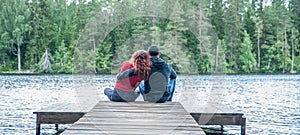 Guy and a girl sit hugging on the pier of a beautiful lake. The concept of love, the summer mood , banner