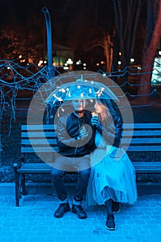 Guy and girl sitting on a bench under an umbrella