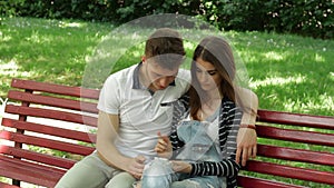 A guy with a girl sitting on a bench and watch pictures on phone