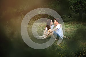 A guy and a girl are sitting on the grass and looking at each other in the park