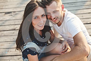 Guy and girl, are sitting on a wooden pier.