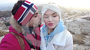 A guy and a girl stand on the edge of a rock in an embrace in winter and kiss joy appears on their faces