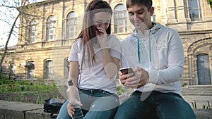 Guy and girl, students, sit in the park, shoot the video in the phone and laugh