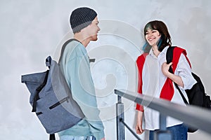 Guy and girl, teenage students with backpacks, standing talking indoors
