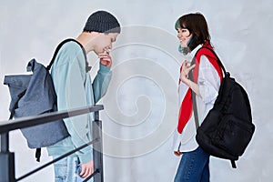 Guy and girl, teenage students with backpacks, standing talking indoors