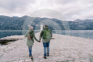 Guy and girl walk holding hands to the lighthouse on the pier. Back view