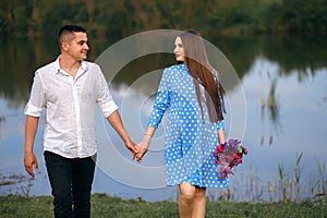 A guy and a girl are walking along the riverbank, holding hands, a girl with flowers, Valentine`s Day